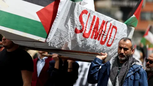 محتجون يحملون نعشًا مكتوبًا عليه "صمود" خلال مظاهرة تضامن مع غزة، مع أعلام فلسطينية ترفرف في الخلفية.