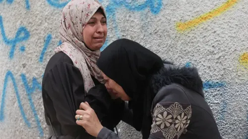 امرأتان ترتديان الحجاب، تعبران عن حزن عميق أثناء تأبين أحد الضحايا في غزة، وسط جدران ملونة تحمل رسومات.