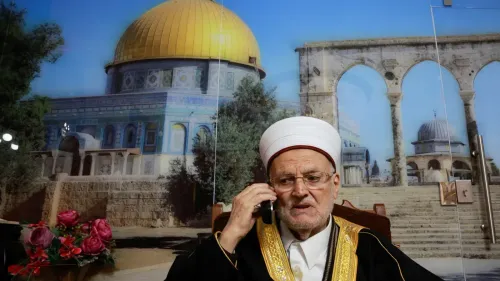 الشيخ عكرمة صبري، إمام المسجد الأقصى، يتحدث عبر الهاتف أمام صورة للمسجد، وسط سياق محاكمته بتهمة "التحريض".