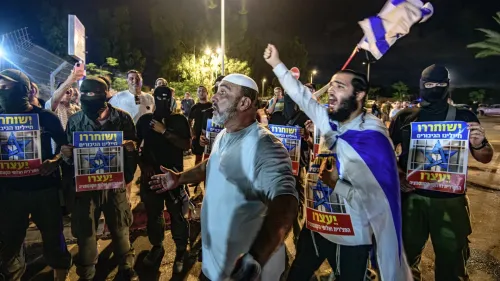 محتجون إسرائيليون يحملون لافتات ويهتفون في مظاهرة ليلية، مع وجود شخص يرتدي غطاء رأس أبيض في المقدمة، تعبيرًا عن القضايا السياسية في المنطقة.