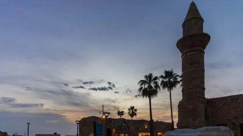 مئذنة مسجد قديمة عند الغروب مع أشجار النخيل، تعكس أهمية الأذان في الهوية الإسلامية وسط الجدل حول قانون مكبرات الصوت في إسرائيل.