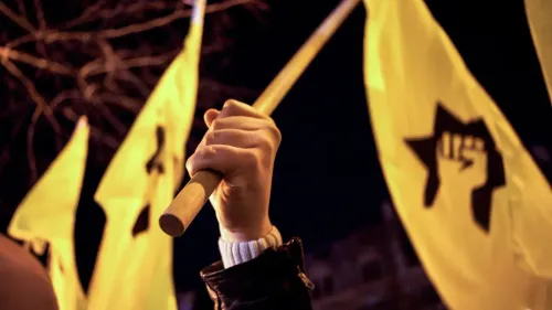 يد تحمل عصا وتلوح بأعلام صفراء، تعبيرًا عن الاحتجاج أو التأييد، في سياق الأحداث المتعلقة بكرة القدم في إسرائيل.