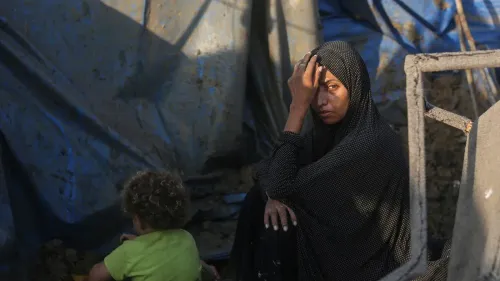 امرأة فلسطينية ترتدي الحجاب تجلس بحزن وسط أنقاض منزلها في غزة، تعكس تداعيات الهجمات الإسرائيلية المستمرة على القطاع.