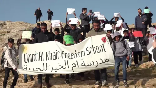 طلاب فلسطينيون في قرية أمّ الخير يحملون لافتات خلال احتجاج للمطالبة بحقهم في التعليم، وسط انتشار قوات الاحتلال الإسرائيلي.