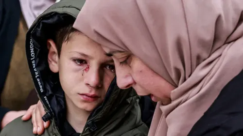 طفل مصاب بجروح في وجهه يتلقى الدعم من امرأة ترتدي الحجاب، مع تعبيرات حزينة تعكس الألم والمعاناة بعد حادث مأساوي.