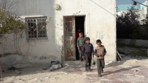 أطفال فلسطينيون يخرجون من منزل قديم في بلدة الريحية، يظهر الباب المكسور والواجهة المتآكلة، تعبير عن الظروف الصعبة التي يعيشونها.