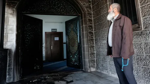 رجل يقف أمام مدخل مسجد أبو بكر الصديق المحترق في قرية تل، حيث تظهر آثار الحريق على الأبواب والجدران.