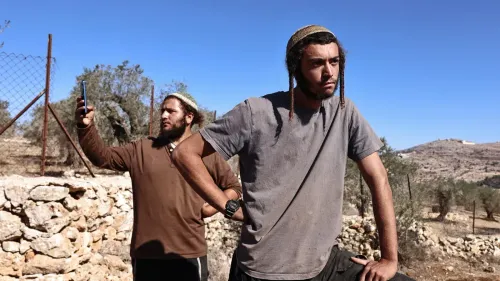 مستوطنون إسرائيليون يقفون بالقرب من سياج في الضفة الغربية، يعكسون التوترات المتزايدة مع الفلسطينيين في المنطقة.