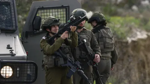 جندي إسرائيلي يحمل سلاحًا، مبتسمًا، بينما يقف بجانب زملائه في موقع عسكري، مما يعكس التوترات الأمنية في المنطقة.