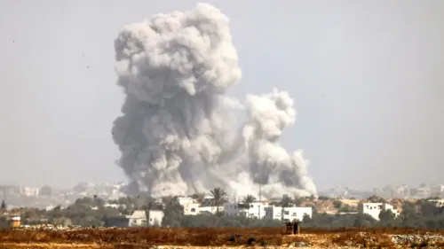 سحابة ضخمة من الدخان تتصاعد في سماء غزة بعد انفجار، مع بيوت فلسطينية في الخلفية، تعكس آثار الصراع المستمر.