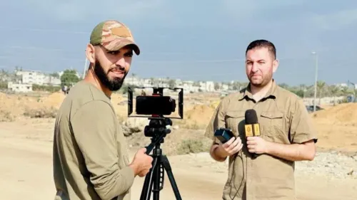 صحفيان فلسطينيان في مخيم البريج بغزة، أحدهما يحمل ميكروفوناً والآخر يقف أمام كاميرا، يعكسان تحديات العمل الصحفي في ظل النزاع.