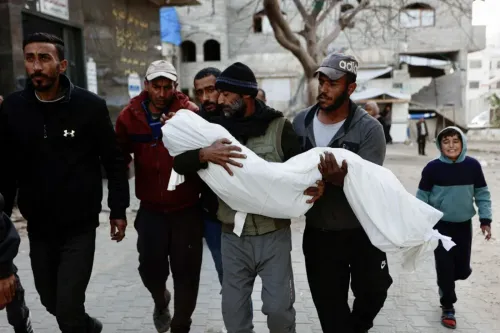 رجال يحملون جثمان طفل مغطى ببطانية بيضاء في شوارع غزة، مع وجود طفل صغير يبتسم في الخلفية، في سياق الغارات الإسرائيلية.