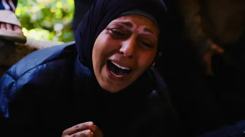 امرأة ترتدي الحجاب تعبر عن حزن عميق أثناء تأبين ضحايا الحرب في غزة، مع خلفية غير واضحة تعكس مشاعر الألم والمعاناة.