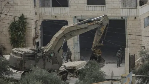 جرافة تعمل على هدم مبنى في الضفة الغربية المحتلة، بينما يتواجد جنود إسرائيليون في المنطقة، مما يعكس تصعيد عمليات التهجير والمصادرة.