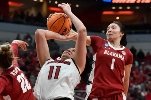 لاعبة كرة سلة من فريق لويزفيل تحاول تسجيل نقطة بينما تتصدى لها لاعبة من فريق ألاباما خلال مباراة NCAA المثيرة.