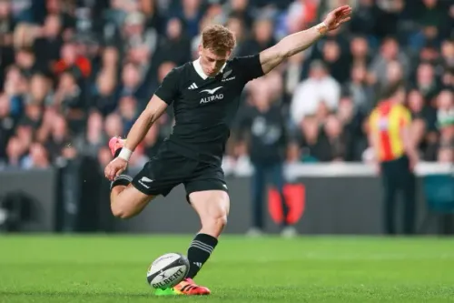 لاعب رغبي نيوزيلندي من فريق All Blacks يركل الكرة خلال مباراة اختبار ضد جنوب أفريقيا، مع جمهور في الخلفية.