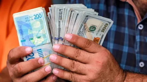 رجل يحمل مجموعة من الأوراق النقدية، تشمل شيكل إسرائيلي فئة 200 ودولارات أمريكية، في سياق الأزمات المالية التي تواجهها الأراضي الفلسطينية.