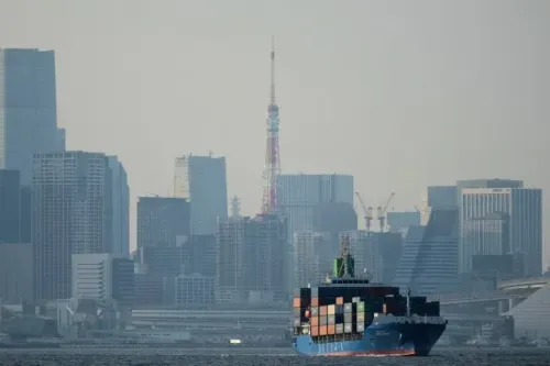 سفينة شحن محملة بالحاويات تبحر في مياه طوكيو، مع ظهور معالم المدينة الحديثة في الخلفية، تعكس نشاط الصادرات اليابانية.