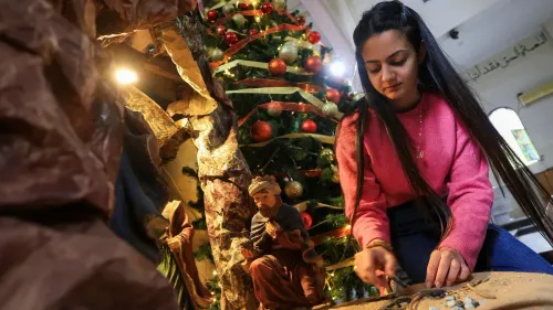 امرأة ترتب تماثيل الميلاد أمام شجرة عيد الميلاد في كنيسة بالقدس، تعبيرًا عن الاحتفال بالعيد وسط التحديات التي تواجه المجتمع المسيحي.