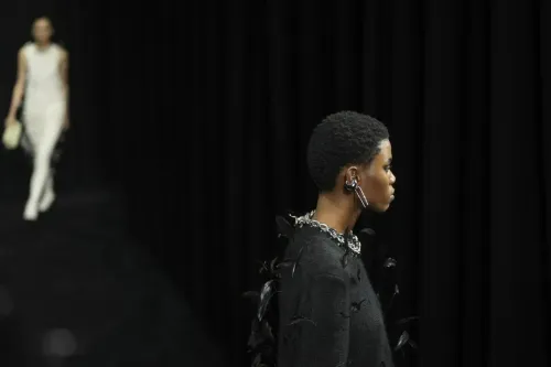 عرضت عارضة أزياء ترتدي ملابس سوداء مزينة بتفاصيل فضية وريش، بينما تظهر عارضة أخرى في الخلف بفستان أبيض.