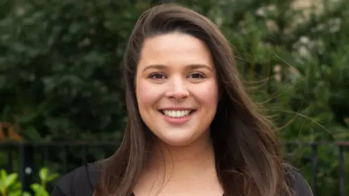 إيزي لينغا، عضوة في مجلس مدينة لندن، تظهر مبتسمة في صورة رسمية، مع خلفية خضراء، تمثل دورها في السياسة المحلية.