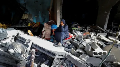 امرأة ترتدي ملابس سوداء تجلس على حطام مبنى مدمر في غزة، تعكس معاناتها في ظل الأوضاع الإنسانية الصعبة.