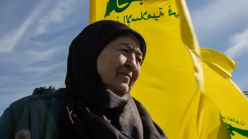 امرأة مسنّة تدعى فاطمة جعفر، تقف أمام أعلام حزب الله في قرية يارون اللبنانية، تعبر عن روح التحدي والأمل وسط التوترات الحدودية.