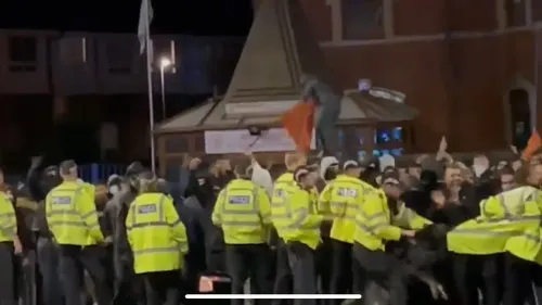 اشتباكات بين الشرطة ومحتجين في ليستر، حيث يظهر ضباط يرتدون سترات صفراء وسط حشود متوترة، تعكس تصاعد العنف الطائفي في 2022.