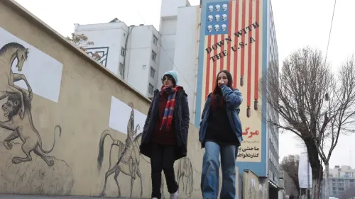 امرأتان تسيران بجوار جدارية تحمل عبارة "الموت لأمريكا" مع رموز تعبيرية، تعكس التوترات السياسية في إيران.