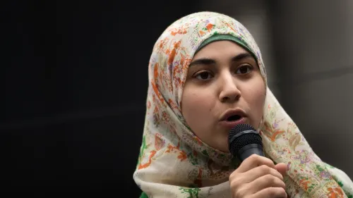 أبير كاواس، مرشحة ديمقراطية من حي كوينز في نيويورك، تتحدث في حدث سياسي، مرتدية الحجاب، مع ميكروفون في يدها.