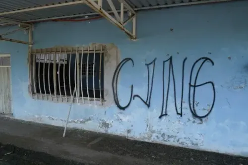 جدار بلون أزرق مع نافذة محمية، مزين برسومات جرافيتي تحمل اسم "CJNG"، تشير إلى وجود كارتل المخدرات في المنطقة.