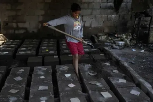 شاب يعمل في مصنع لإنتاج أواني الطهي من الألومنيوم في فنزويلا، محاط بأشكال الأواني الجاهزة.