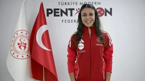 الرياضية التركية İlke Özyüksel Mihrioğlu مبتسمة ترتدي زيًا رياضيًا أحمر أمام علمي تركيا وشعار الاتحاد التركي للخماسي الحديث.