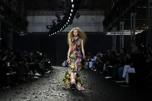 عارضة أزياء تسير على منصة عرض أزياء موسكينو، ترتدي فستانًا مزخرفًا بالألوان الزاهية، مع جمهور يشاهد من الجانبين.