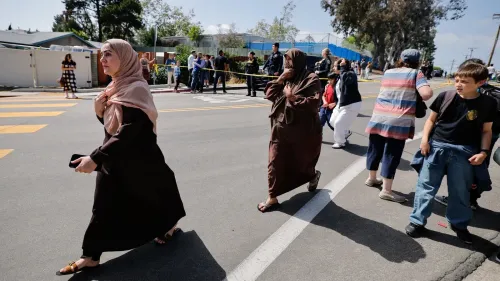 نساء وأطفال يهربون من موقع الهجوم على المركز الإسلامي في سان دييغو، مع وجود رجال شرطة في الخلفية، مما يعكس حالة من الفوضى والخوف.