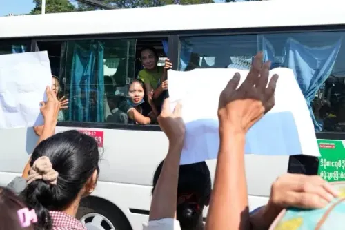 سجناء يلوحون بأيديهم من نافذة حافلة أثناء إطلاق سراحهم في ميانمار، وسط تجمع حشود من الأصدقاء والعائلات المحتفلين.