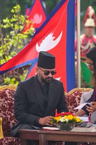 باليندرا شاه، أصغر رئيس وزراء نيبال، يجلس خلال مراسم أداء اليمين الدستورية، مع أعلام نيبالية خلفه وزهور أمامه.