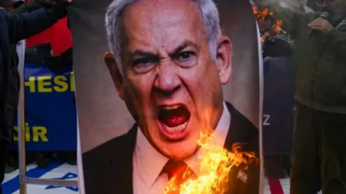 شخص يحمل لافتة مشتعلة تظهر صورة لرئيس الوزراء الإسرائيلي بنيامين نتنياهو، يعبر عن الاحتجاج والغضب خلال تظاهرة.