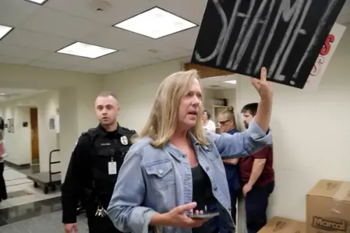 امرأة تحمل لافتة مكتوب عليها "عار" بينما تتحدث، مع وجود ضابط شرطة في الخلفية، في سياق احتجاج حول إعادة رسم دوائر الانتخابات في نورث كارولينا.