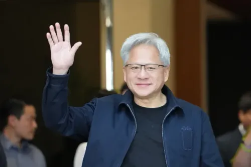 Jensen Huang، الرئيس التنفيذي لشركة Nvidia، يلوح بيده بابتسامة، مع خلفية غير واضحة، مما يعكس دوره في تعزيز الابتكار في الذكاء الاصطناعي.