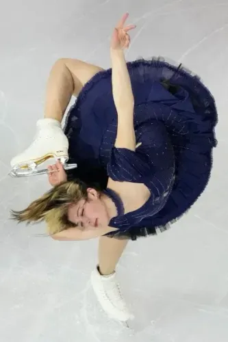 أليسا ليو، البطلة الأولمبية في التزلج على الجليد، تؤدي حركة رائعة أثناء المنافسة، مرتدية فستاناً أزرق داكن مزيناً.