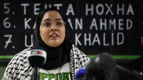 ناشطة ترتدي حجابًا وتلقي كلمة دعم للناشط كمران أحمد، مع وجود لافتات خلفها تحمل أسماء معتقلين آخرين.