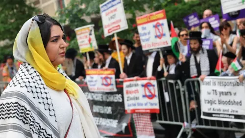 ناشطة فلسطينية-أمريكية ترتدي حجابًا وتظهر في مظاهرة، محاطة بلافتات تعبر عن دعم فلسطين، تعكس التوترات حول حقوق الفلسطينيين.