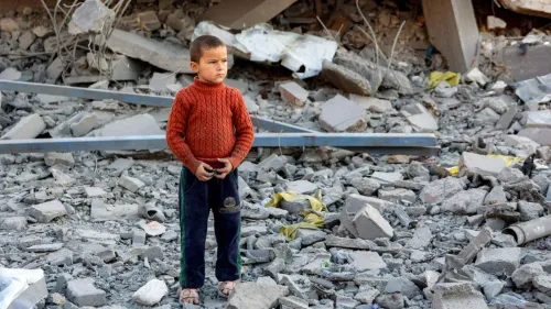 طفل فلسطيني يقف وحيدًا بين أنقاض مبنى مدمّر، يعكس معاناة الأطفال في ظل الصراع المستمر والضغوط على منظمات حقوق الإنسان.