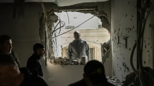 شخص ينظر من خلال فتحة في جدار مدمّر، بينما يتجمع آخرون في الداخل، مما يعكس آثار الصراع والدمار في المجتمعات الفلسطينية.