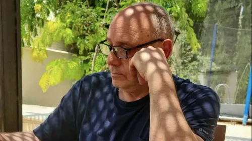 الطبيب الفلسطيني ماجن رنتيسي يجلس متأملاً في ظل شجرة، معظمه في ضوء الشمس، يعكس حالة الإهمال الطبي وظروف الاعتقال القاسية التي يواجهها في سجن عوفر.