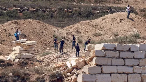 أشخاص فلسطينيون يقفون على تلة قرب بقايا جدار مهدّم في قرية قصرة بالضفة الغربية، في سياق حصار المستوطنين الإسرائيليين للمنازل الفلسطينية.