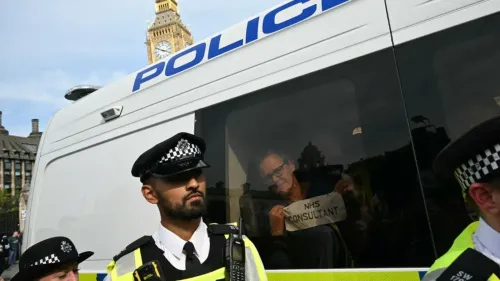 شرطيان يقفان أمام سيارة شرطة بينما يحمل شخص داخلها لافتة مكتوب عليها "استشاري NHS"، مع برج ساعة بيغ بن في الخلفية.