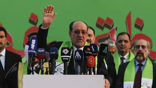 نوري المالكي يتحدث في تجمع سياسي، محاطًا بمؤيديه، مع خلفية خضراء، مما يعكس نشاطه السياسي المستمر في العراق.