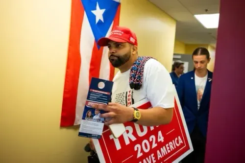 رجل يحمل لافتة لدعم ترامب 2024، يتواجد بالقرب من علم بورتو ريكو، في إطار حملة تواصل مع الناخبين اللاتينيين.